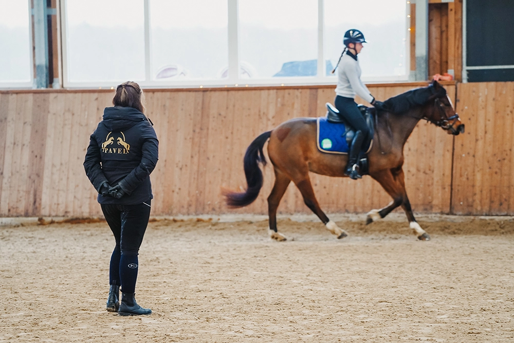 Trainerin beobachtet Reitschülerin auf Pferd in Reithalle