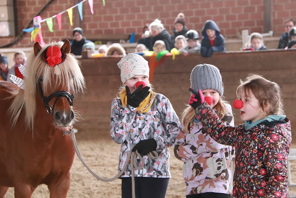 Kinder mit Faschingsnasen neben Pferd in Reithalle, Publikum im Hintergrund
