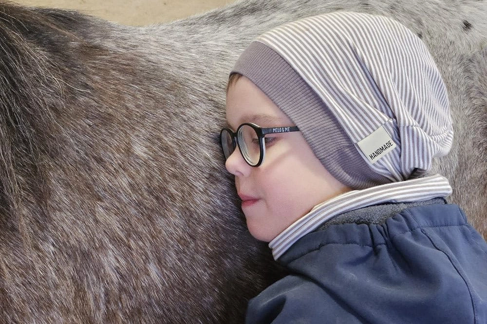 Kind legt seinen Kopf an den Rücken eines Pferdes