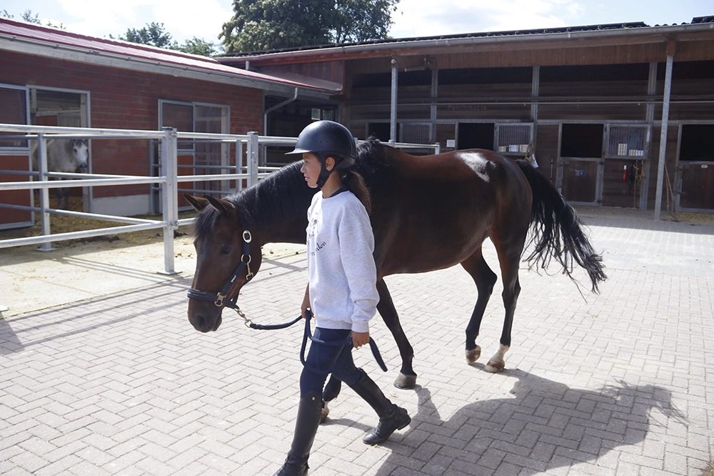 Reitschülerin führt Pferd am Stall vorbei